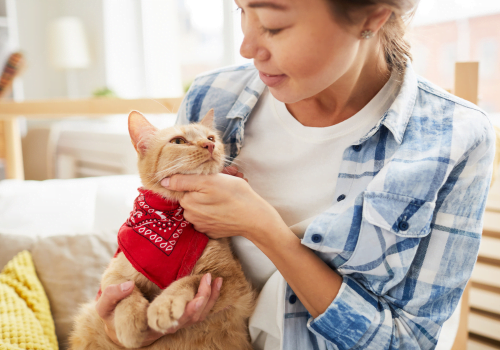 a woman holding a cat wearing a red bandana